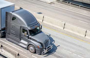 Gray big rig long haul semi truck transporting semi trailer with commercial cargo running on wide...