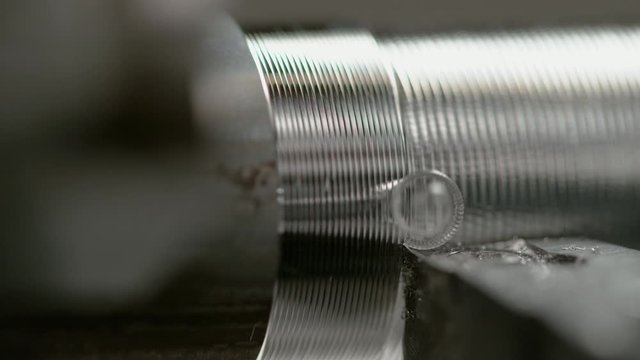 SLOW MOTION MACRO DOF: Detailed shot of a CNC machine threading a small aluminium rod. Twisted chips come flying off a piece of metal during metal shaping process. Lathe tool shaving grooves into rod.