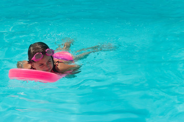 Cute Little girl practices swimming on a kick board in the pool