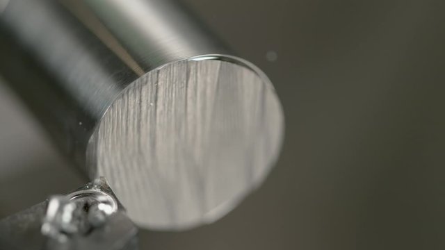 SLOW MOTION, MACRO, DOF: Detailed shot of a lathe tool shaving the edge of a shiny metal rod. Twisted shavings of aluminium spiral off a shiny workpiece processed by a CNC machine. Rotating cylinder