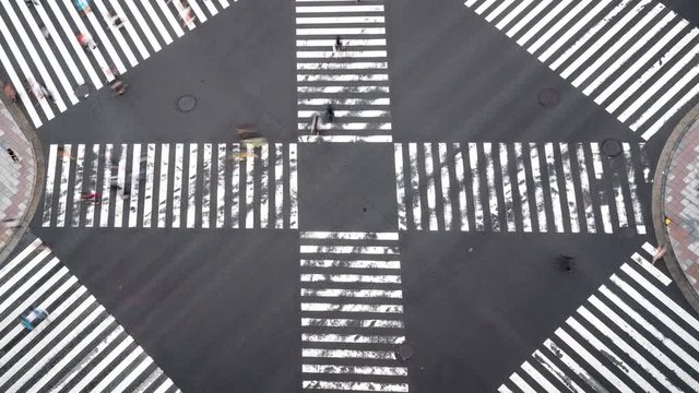 4K Timelapse high angle aerial view zoom out wide shot of pedestrian man and woman walking crossing the street crosswalk with traffic driving cars on the road in summer at Ginza, Tokyo, Japan.