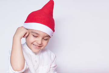 Portrait of smiling shy boy. Six-year-old kid shy and smiling. Celebrating Christmas. 6-7 year old child with Santa hat.