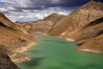 View of Winding Road near Manak Dam Lake from Simila Pass - Gyantse, Shigatse, Tibet Autonomous Region of China. Manla Reservoir, high altitude body of water. Exotic Chinese Landscape