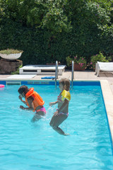 Two little girls jumping together in the pool; positive emotions, summer and fun
