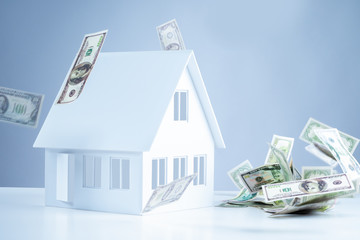The layout of the cottage on the background of falling banknotes. Reduction of real estate prices....