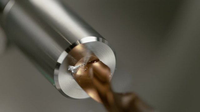SLOW MOTION, MACRO, DOF: Automated lathe tool spot drilling a hole into a shiny cylinder shaped piece of aluminium. Detailed macro shot of a sharp brass drill cutting into the center of a metal rod.