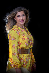 Fashionable Brunette with Flowy Hair Wearing a Floral Yellow Dress in Studio with a Black Backdrop