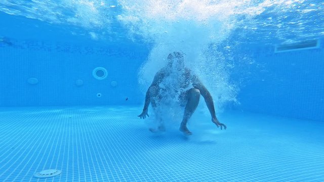 Man jumps under water in the pool. Underwater view on a man diving into water and swimming inside the swimming pool.