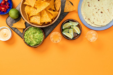 Mexican nachos served on wooden cutting board with guacamole, cheese sauce, peppers, limes, Tequila...