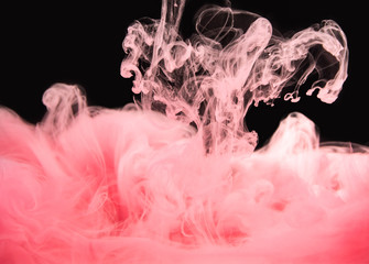 Pink paint dissolving into water, isolated on black background, close up view. Acrylic smoke waving...