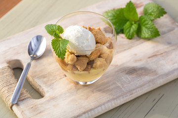 Apple crumble topping vanilla ice cream served with melisa in glass and wooden tray on table.
