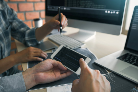 Software developers are using smart phones and analyzing together the code written in the program on the computer.
