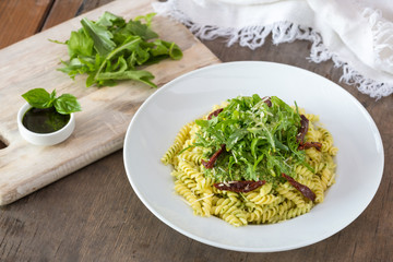 Colored pasta with rukola and basil on white plate with sauce.