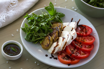 Caprese salad with mozzarella, tomato, basil and grilled eggplant on white plate. Top view on background