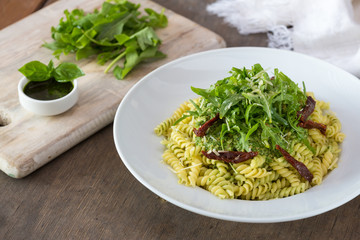 Colored pasta with rukola and basil on white plate with sauce.