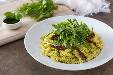 Colored pasta with rukola and basil on white plate with sauce.