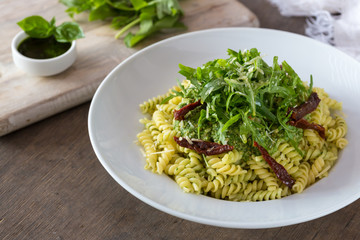 Colored pasta with rukola and basil on white plate with sauce.
