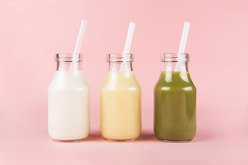 Three bottles with colorful drinks on pink background.