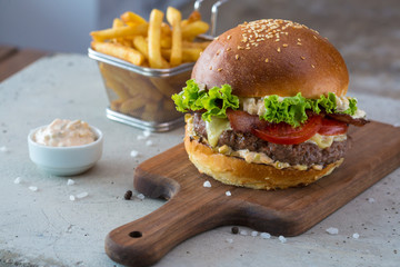 Highigh burger with french fries in small fry basket on concrete surface. Traditional American fastfood.