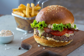 Highigh burger with french fries in small fry basket on concrete surface. Traditional American fastfood.