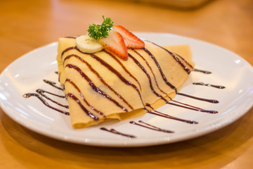 crepe with banana and chocolate,Fresh homemade crepes with strawberries and chocolate sauce on rustic wooden background. Top view.