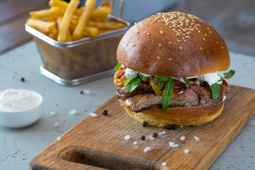Highigh burger with french fries in small fry basket on concrete surface. Traditional American fastfood.