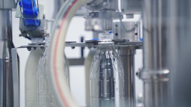 Automated machine covering plastic bottle with lid. Dairy production. Mechanical process of putting cover on a bottle with milk in a modern factory.