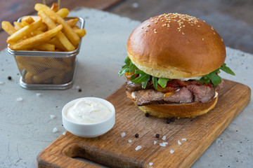 Highigh burger with french fries in small fry basket on concrete surface. Traditional American fastfood.