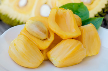 pile of peeled Jackfruit and seed with leaf in white dish, half of jack fruit background.