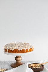 almond olive oil cake with brown butter icing and sliced almonds, dripping icing on cake, marble and wood cake stand, styled bakery