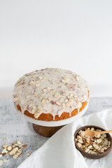Fototapeta na wymiar almond olive oil cake with brown butter icing and sliced almonds, dripping icing on cake, marble and wood cake stand, styled bakery