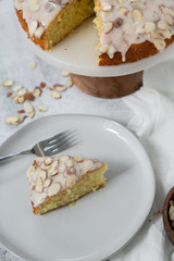 slice of almond olive oil cake with brown butter icing and sliced almonds, dripping icing on cake, marble and wood cake stand, styled bakery