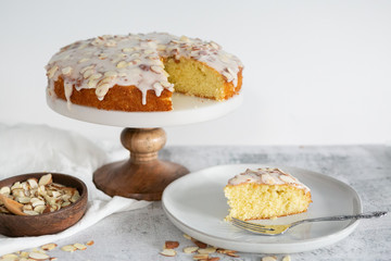slice of almond olive oil cake with brown butter icing and sliced almonds, dripping icing on cake, marble and wood cake stand, styled bakery