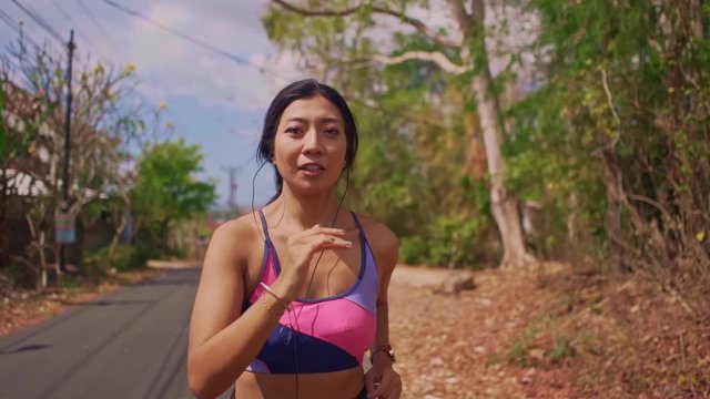 frontal pull back gimbal shot in dolly style of young exotic fit and beautiful Asian Indonesian woman running on asphalt road doing jogging workout in sport and healthy lifestyle concept
