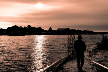 Silhouette of guy in hat fishing in river on sunset