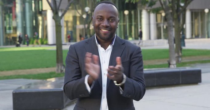 Business man claps while smiling and staring into camera outdoors - slow motion - shot on RED