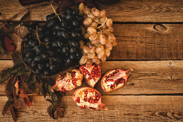 Organic ripe pomegranate fruit and grapes on wooden vintage background. Autumn harvest background. Vintage oriental still life. Toned image. Selective focus.