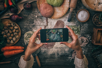 Hands with the smart phone pictures of meal. Young woman, cooking blogger is cooking at the home kitchen and is making photo at smartphone. Instagram food blogger workshop concept.