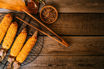 Corn grilled with cheese and spices on the dark rustic background. Autumn food background. Fast food in the summer or fall. Toned image. Flat lay with copy space.
