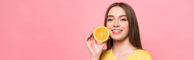 panoramic shot of smiling attractive girl holding cut orange isolated on pink