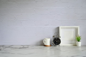Fototapeta na wymiar Copy space alarm clock. coffee, photo frame and plant decoration on white marble table and brick wall.