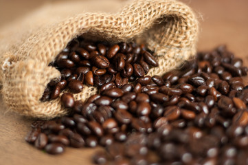 Freshly roasted dark coffee beans out of small jute sack, close up