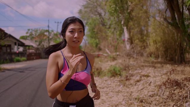 frontal pull back gimbal shot in dolly style of young exotic fit and beautiful Asian Indonesian woman running on asphalt road doing jogging workout in sport and healthy lifestyle concept
