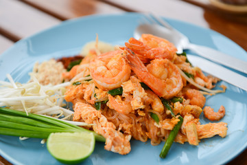 Thai food of noodle Pad Thai with shrimp and side dish including lemon, spring onions and bean sprouts in dish