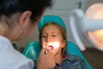 Close up portrait of a little smiling girl at dentist office. Girl at the dentist. Dentist examining little girl's teeth in clinic. people, medicine, stomatology and health care concept