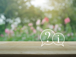 Question mark and information chat icon on wooden table over blur pink flower and tree in garden,...