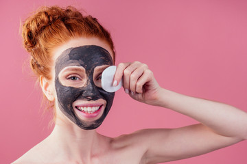 redhaired ginger young caucasian woman with natural anti acne mask on her pretty perfect face in studio pink background .