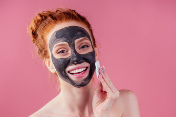 redhaired ginger young caucasian woman with natural anti acne mask on her pretty perfect face in studio pink background