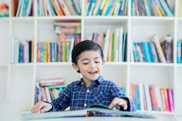 Cute little boy reading a book in the library
