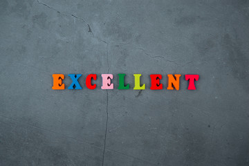 The multicolored excellent word is made of wooden letters on a grey plastered wall background.
